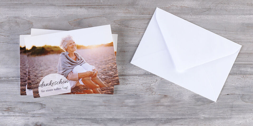 A thank you greeting card lies next to a white envelope on a wooden table