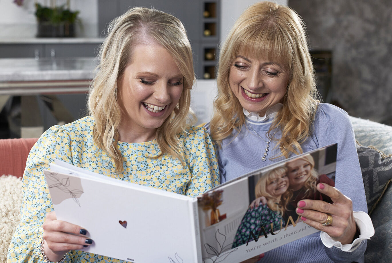 Two people look together at a photo book on the couch.