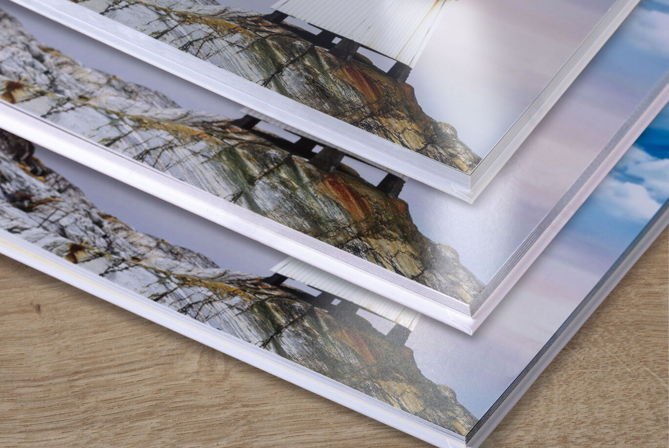 Three stacks of CEWE PHOTO BOOKS with beautiful landscape pictures on the cover, lying on the table.
