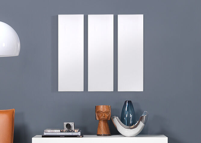 Three empty white frames on a gray wall above a sideboard with decorative objects.
