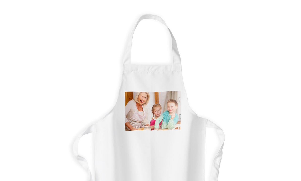 A white apron with a joyful family photo of an older woman and two children baking together.