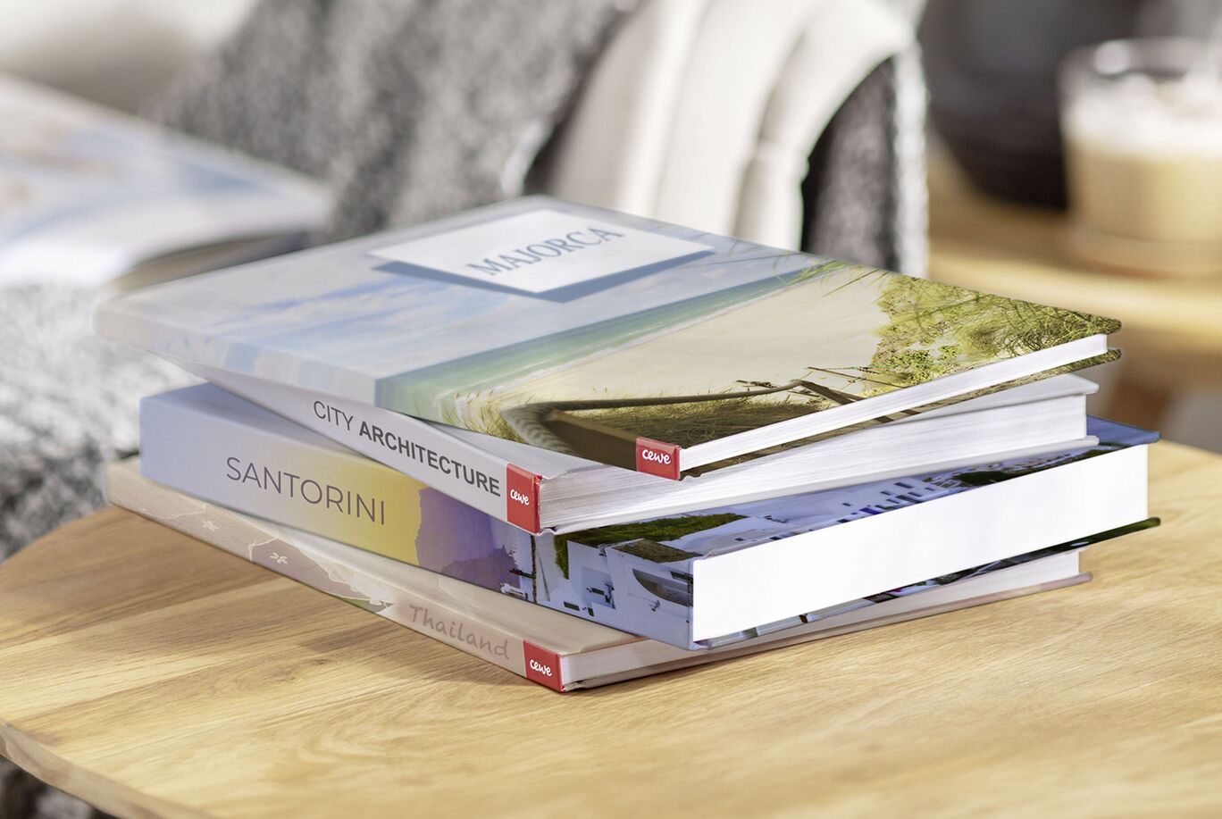 Three stacked CEWE photo books on a table showcasing beautiful landscapes, including Santorini and architecture.