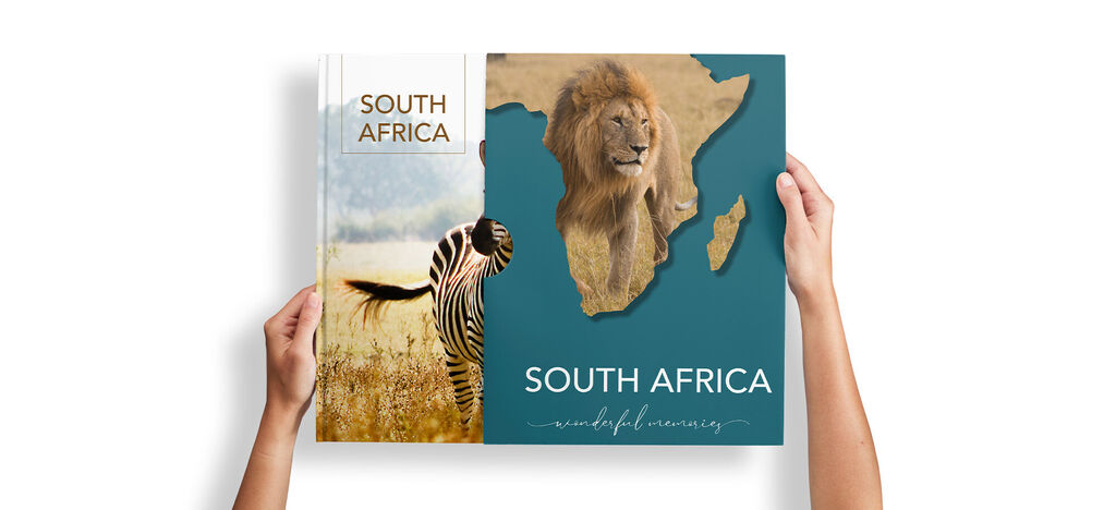 A person holds a CEWE photo book titled 'South Africa', showing a lion image and a map of Africa.