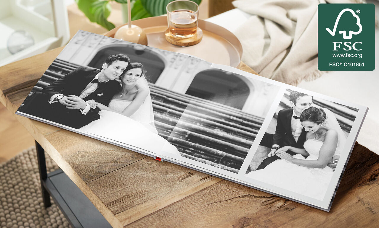 An open photo book with wedding photos on a table. The images show a couple in elegant clothing.