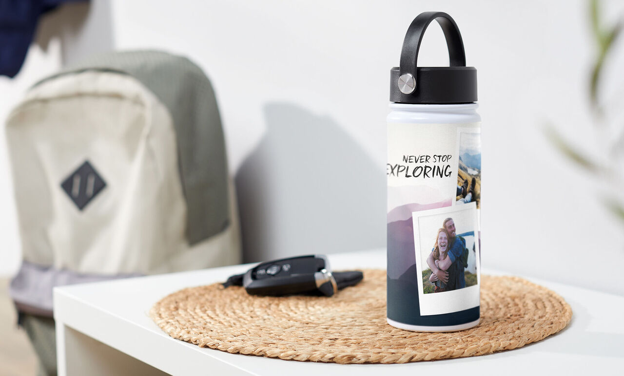 Water bottle featuring text 'Never Stop Exploring' and photos on a table. Background with a backpack and car key.