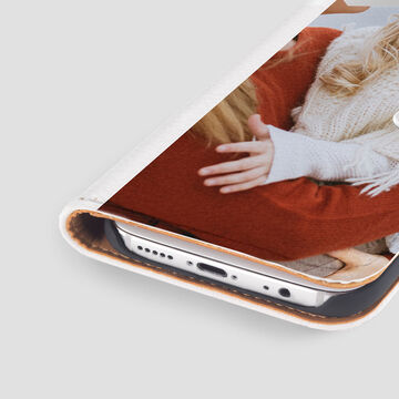 A woman holds her smartphone while sitting in a cozy room on a chair.