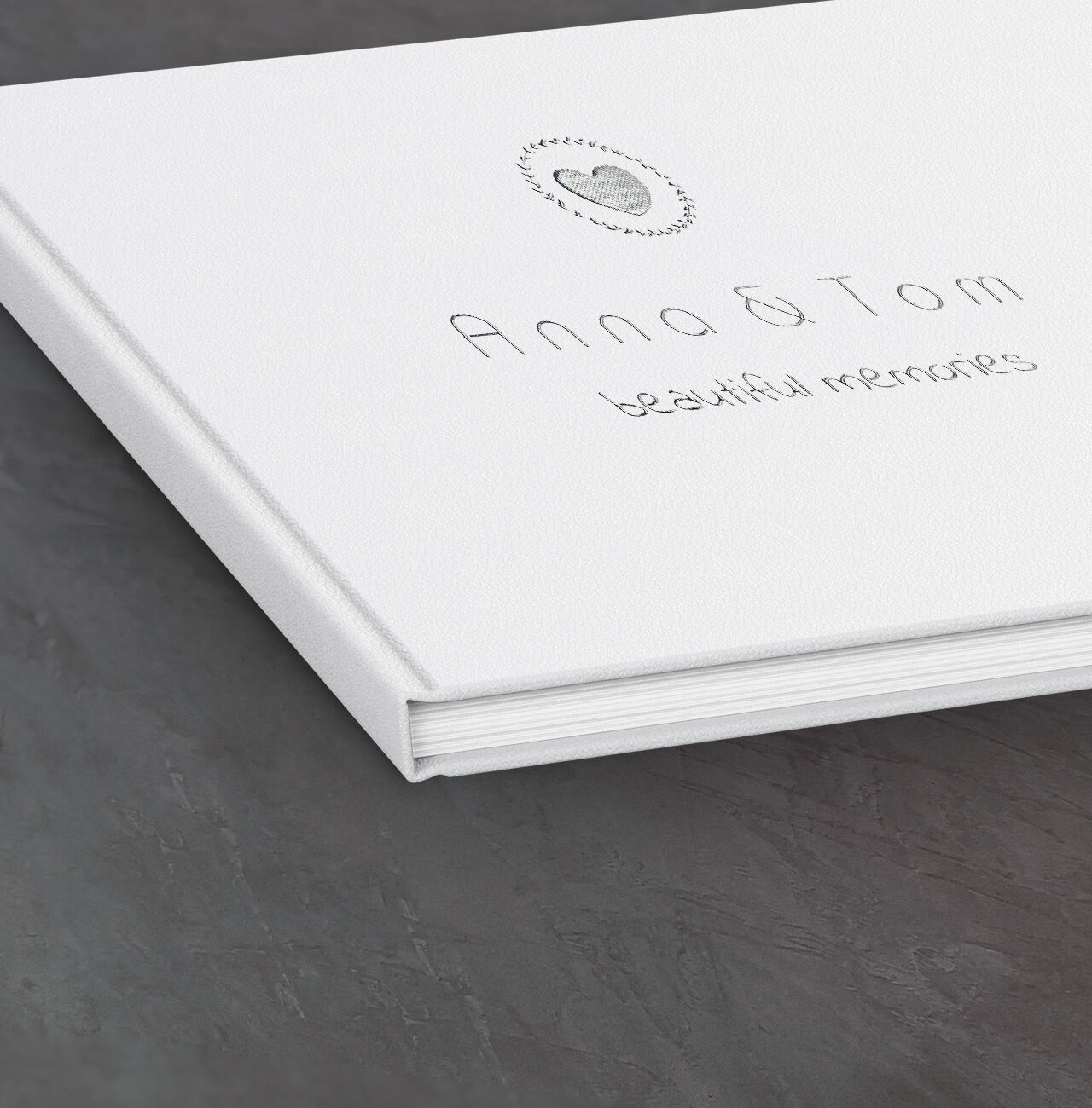 White photo book titled 'Anna & Tom - beautiful memories' on a dark table.