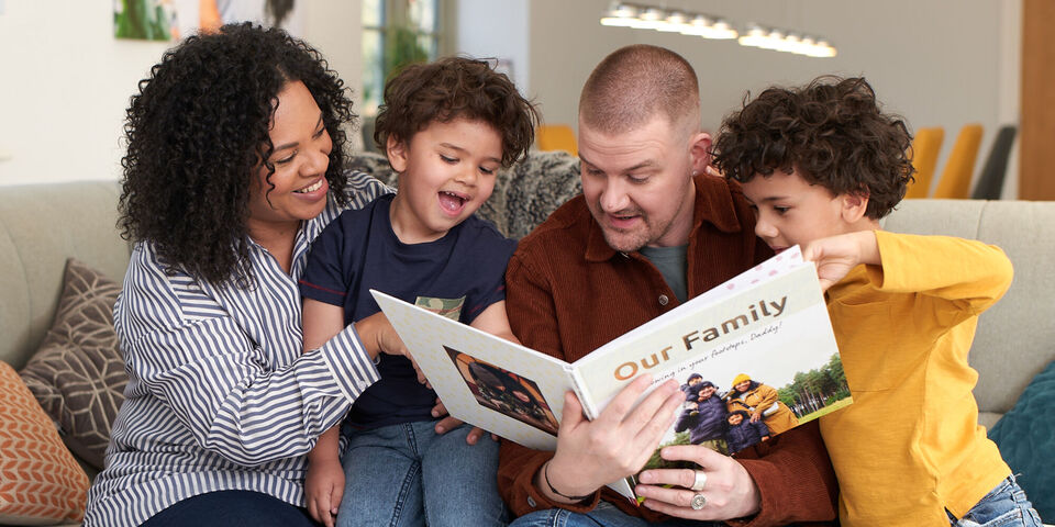 A family sitting on a sofa, looking at a photo book titled 'Our Family'. Everyone looks at it with joy.
