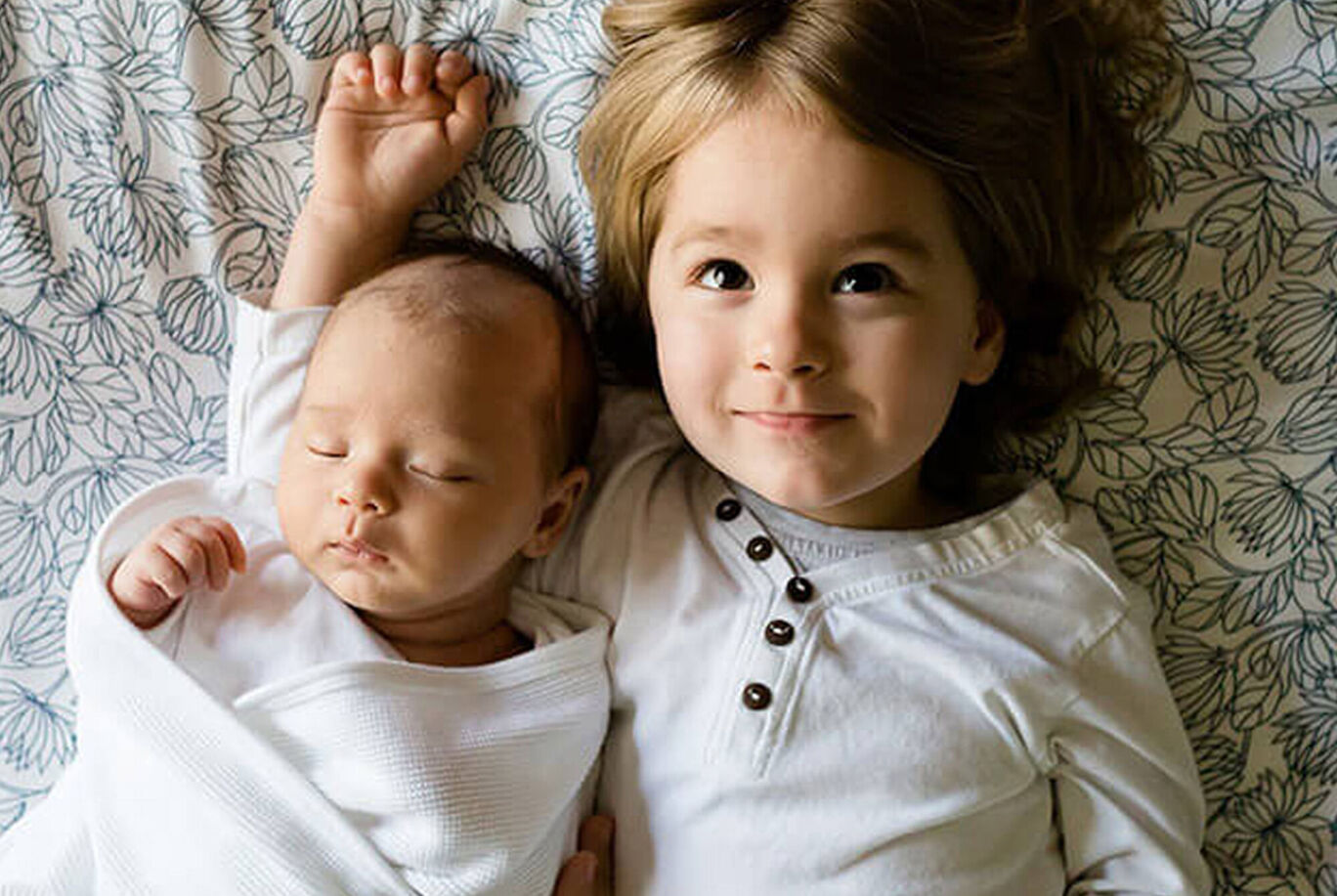 Two children lie relaxed next to each other on floral bedding.