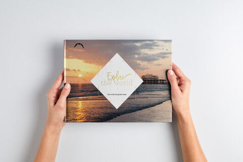 A person holds a CEWE photo book with a beach motif cover.