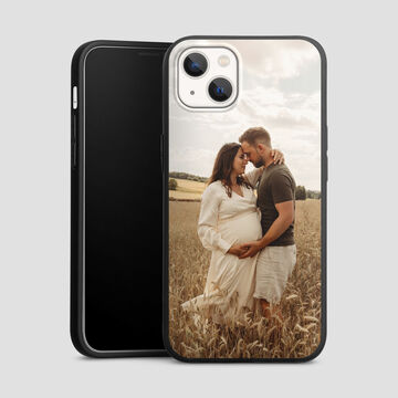 A couple stands in a field embracing. The woman wears a flowing white dress and is pregnant. Behind them is a beautiful landscape with gentle hills and trees.