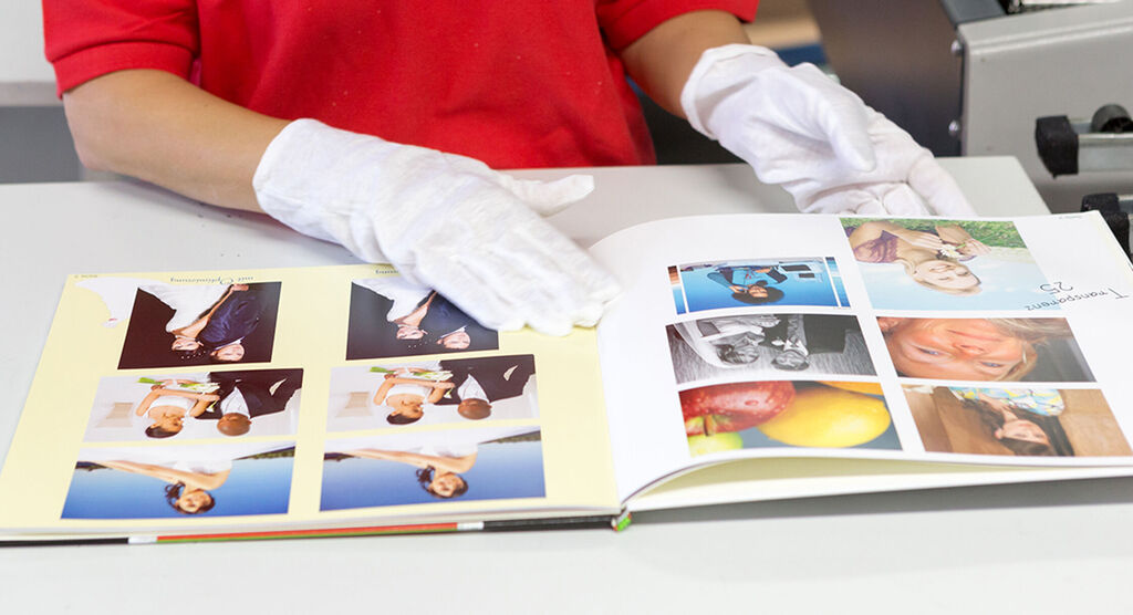 A person flips through a CEWE photo book filled with wedding photos and colorful fruit.