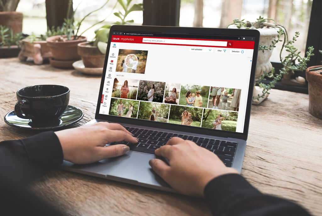 Person at a laptop, viewing photos while a traditional coffee cup sits on the table.