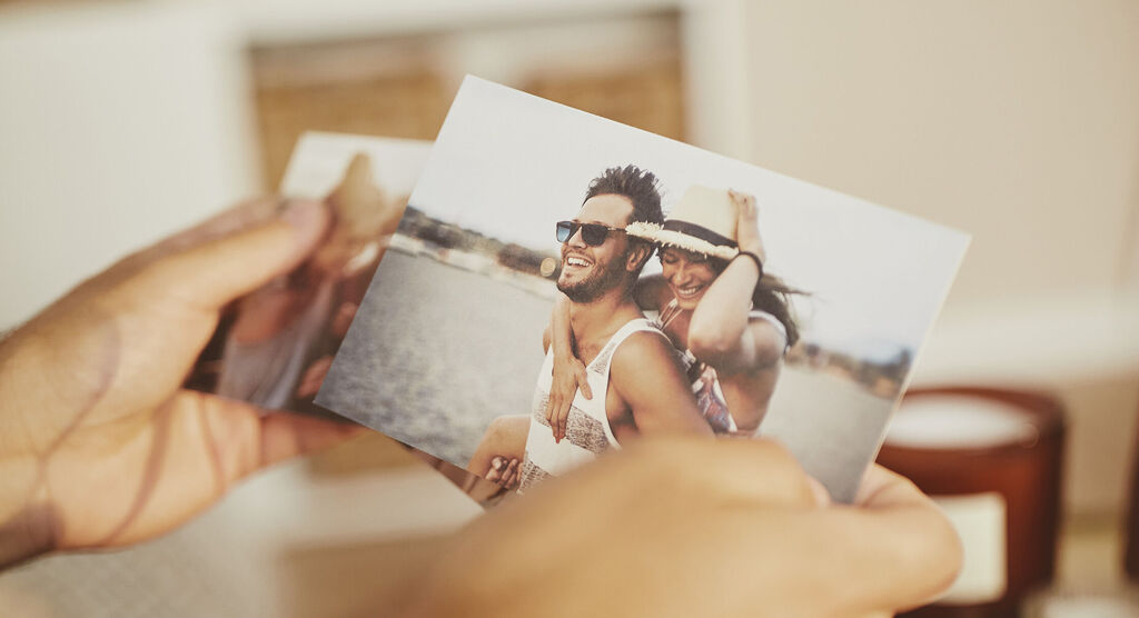 Hands holding two photographs of joyful moments by the water