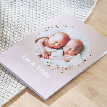 Two newborn twins in a loving photo book design with stars and names, on a bright background.