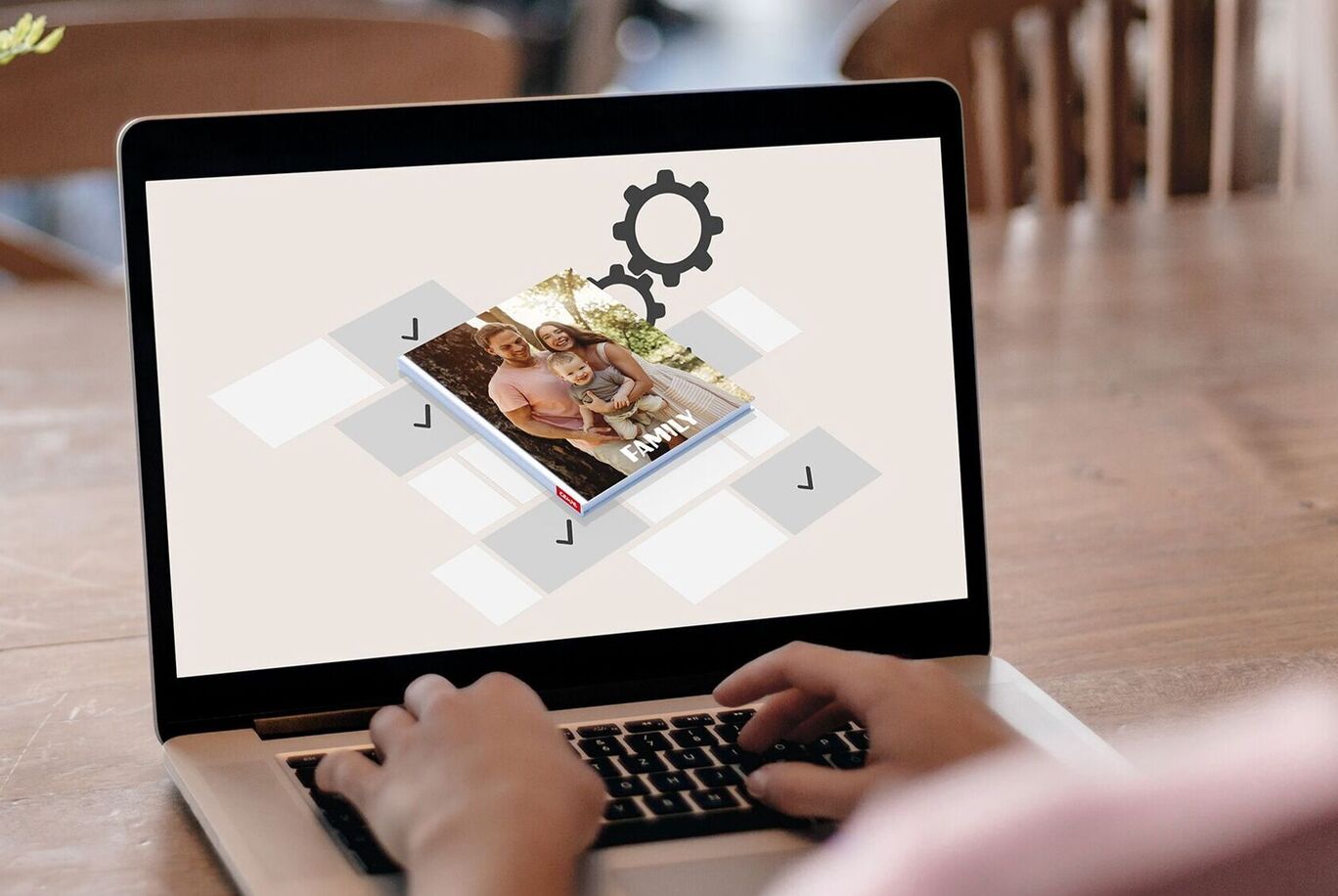 Person designs a CEWE PHOTO BOOK on a laptop with pictures on a table.