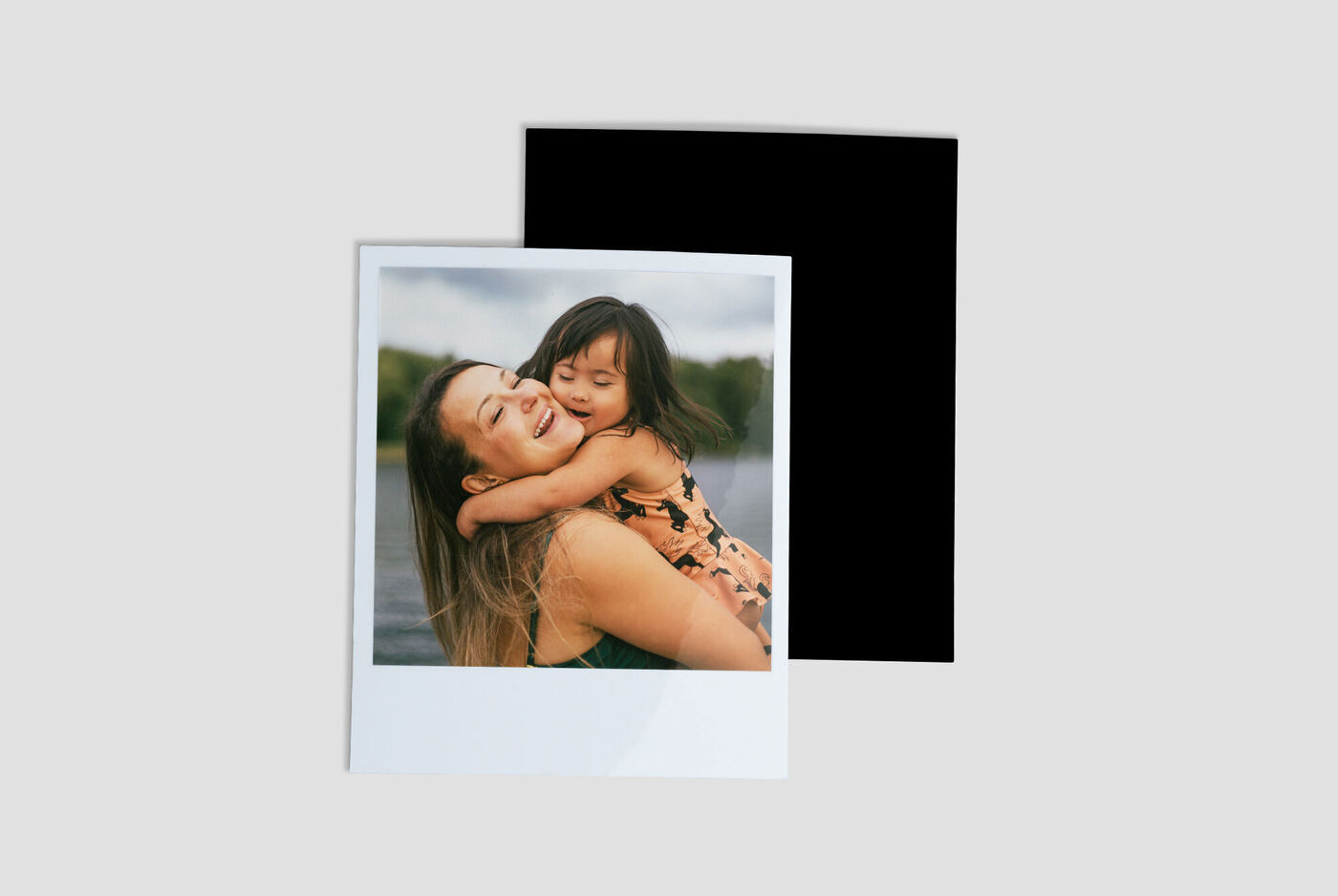 A mother hugs her child by the water, both smiling with joy.
