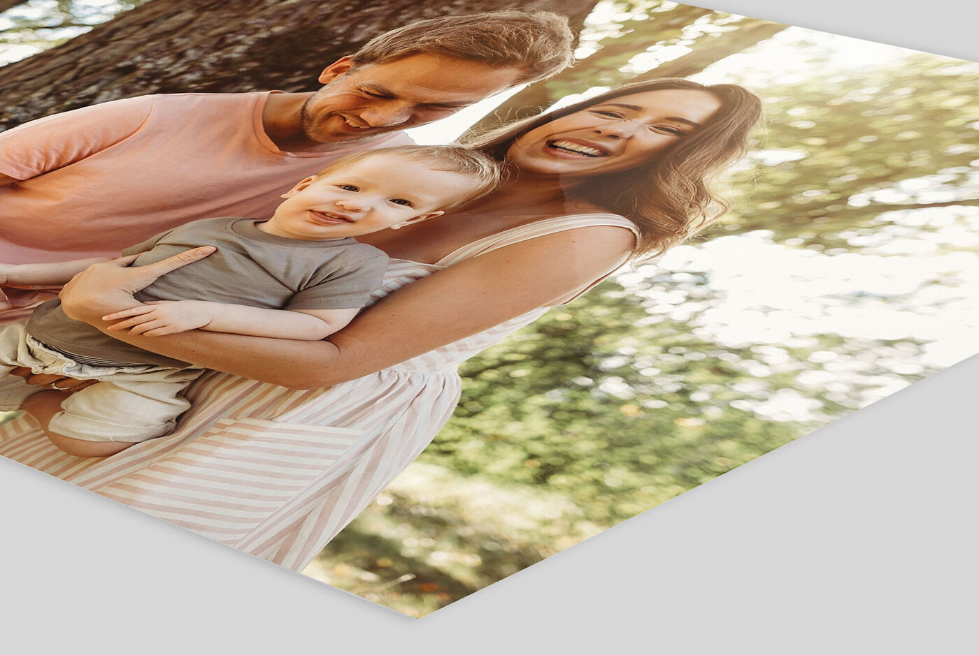 A happy family outdoors, laughing and enjoying a great time. A parent holds a small child while smiling at the camera.