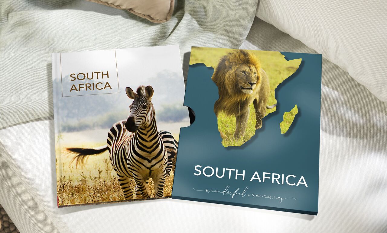 Two photo books titled 'South Africa' on a table, one shows a zebra, the other a lion on the Africa map