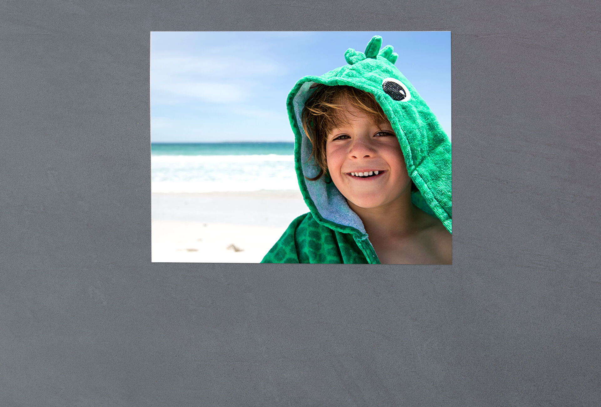 A child wears a green hoodie on the beach and enjoys the sun.