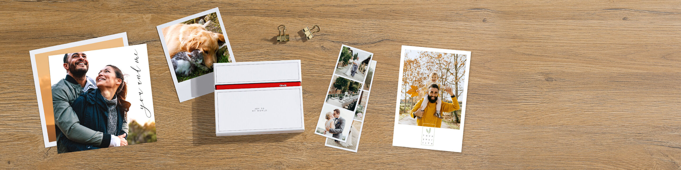 Four personal photo prints lie on a wooden table, surrounded by small clips. The images show happy moments of two people. A CEWE photo calendar is placed in the middle.