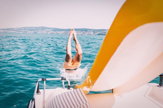 A person happily jumps into the water, legs down, while a yellow slide is visible in the foreground.