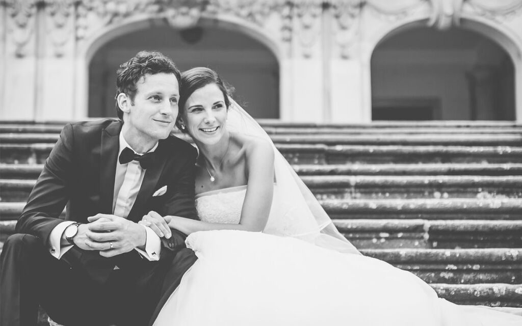 Wedding photo of a bride and groom on stairs, both smiling and happy