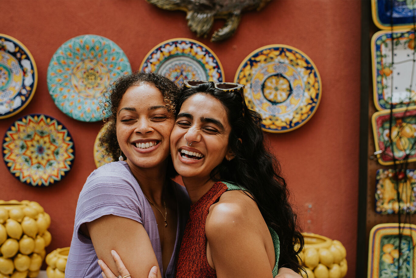 Two women embracing in front of colorful decorative ceramic plates.