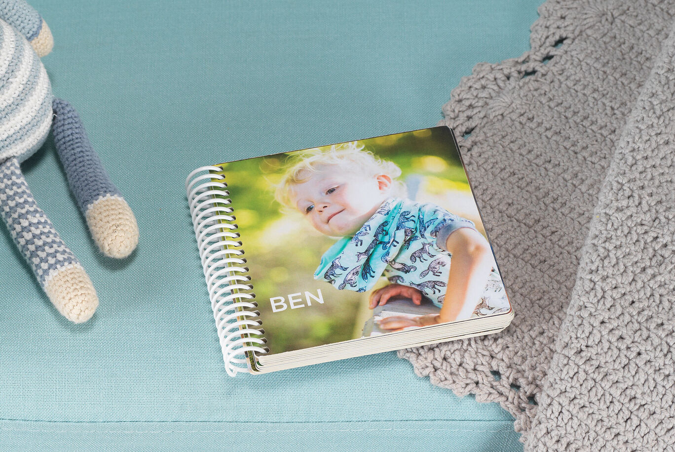 A small photo book titled 'BEN' lies on a light blue couch. A cute boy smiles on the cover.