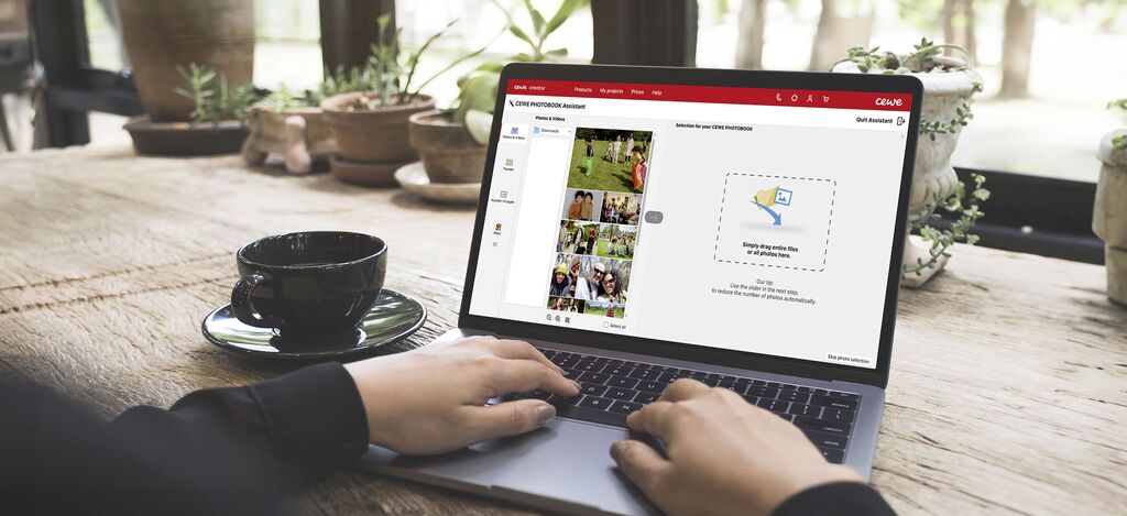 A user working on a laptop to design CEWE photo products, surrounded by plants and a cup of coffee.