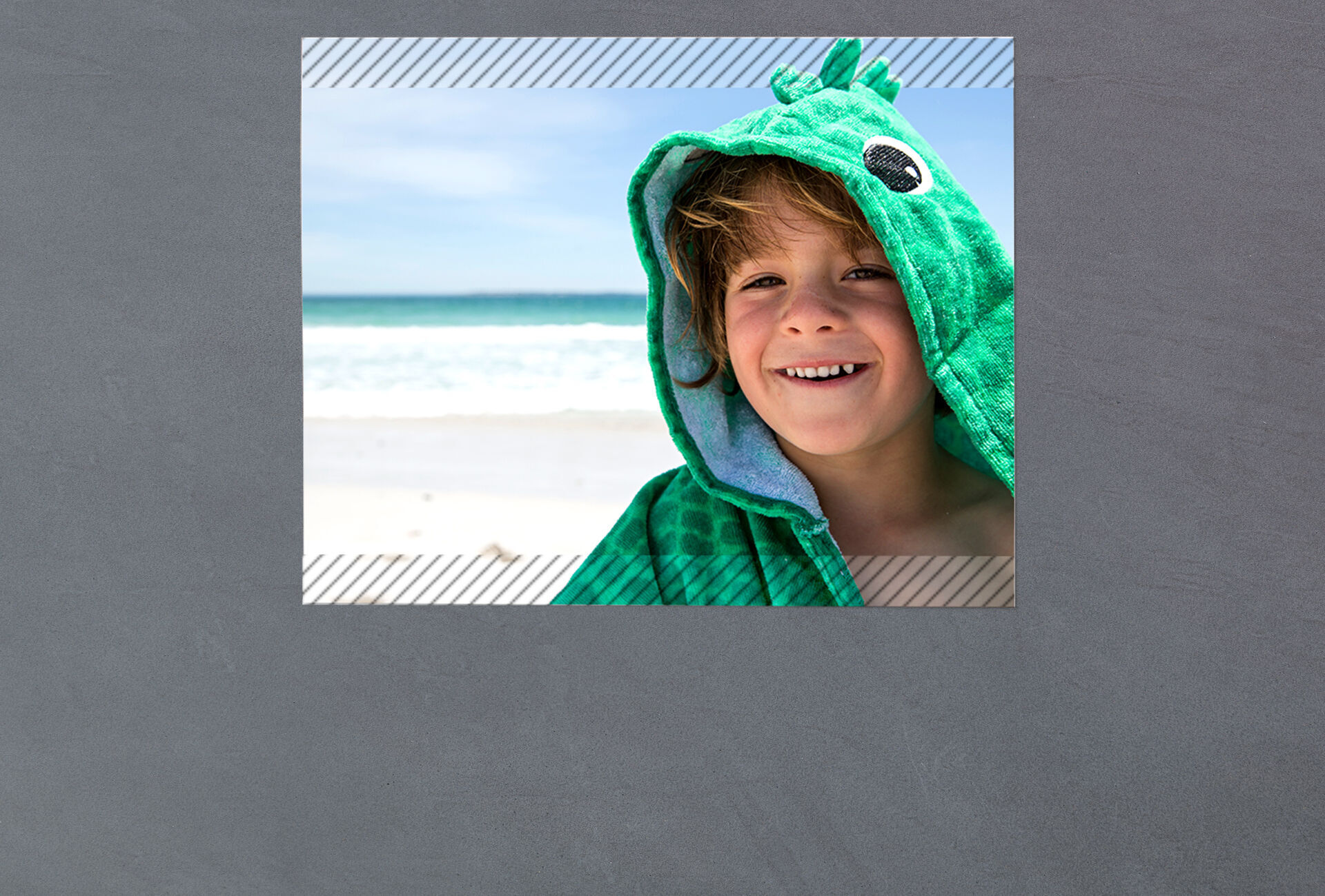 A child in a green animal towel stands on the beach enjoying the day.