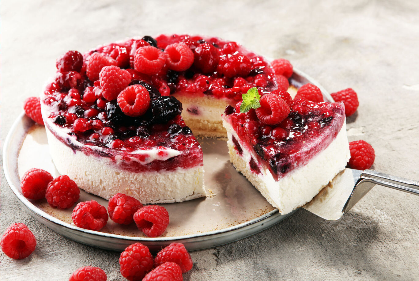 A delicious raspberry cheesecake with fresh raspberries and a fruity glaze, on a silver tray.