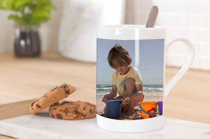 A cup featuring a photo of a child playing with sand at the beach.