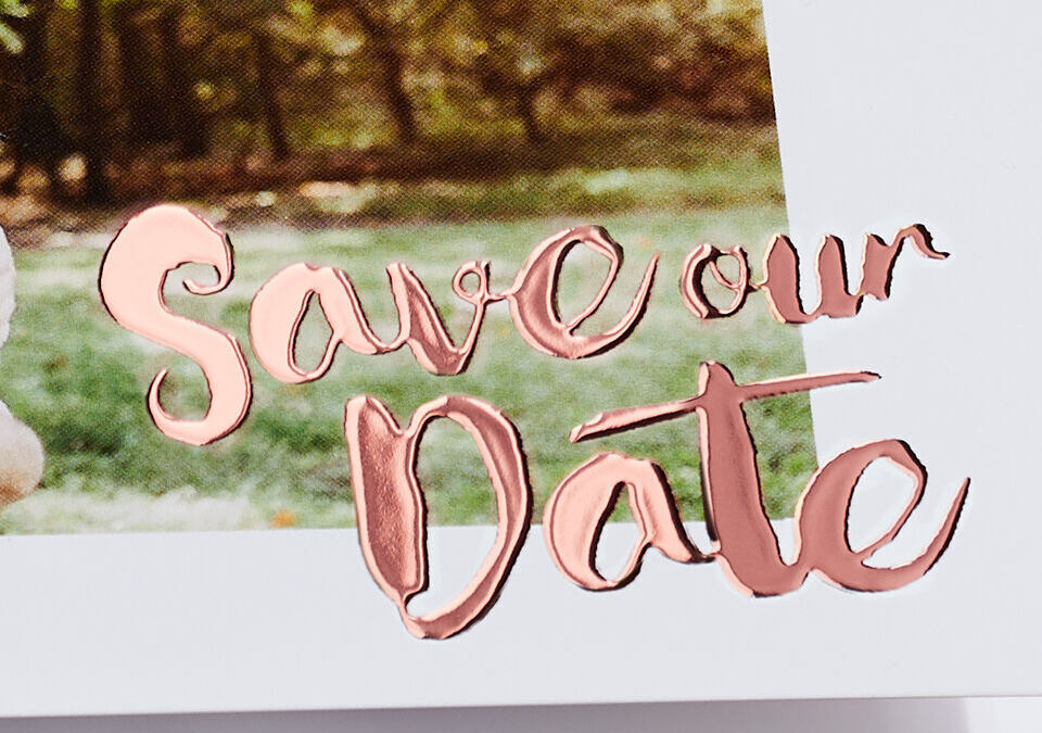 Handwritten 'Save our Date' text in rose gold on a white background with green grass and trees behind.