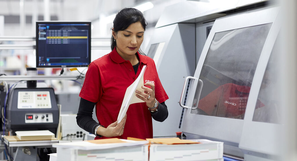 Woman in a red shirt checks a print file next to a machine
