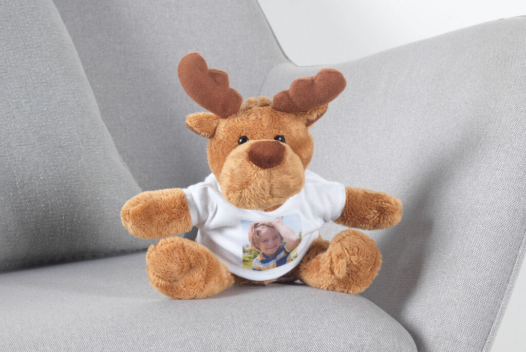 Stuffed animal with horns, wearing a T-shirt with a photo, sitting on a light gray sofa.