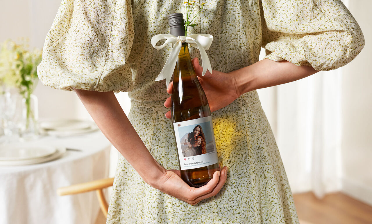 A person holds a wine bottle with a personalized label featuring a picture and text.