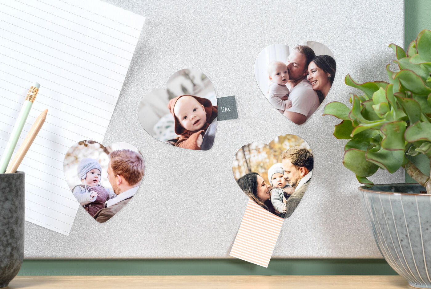 Four heart-shaped photos on a table with a green plant and notepads
