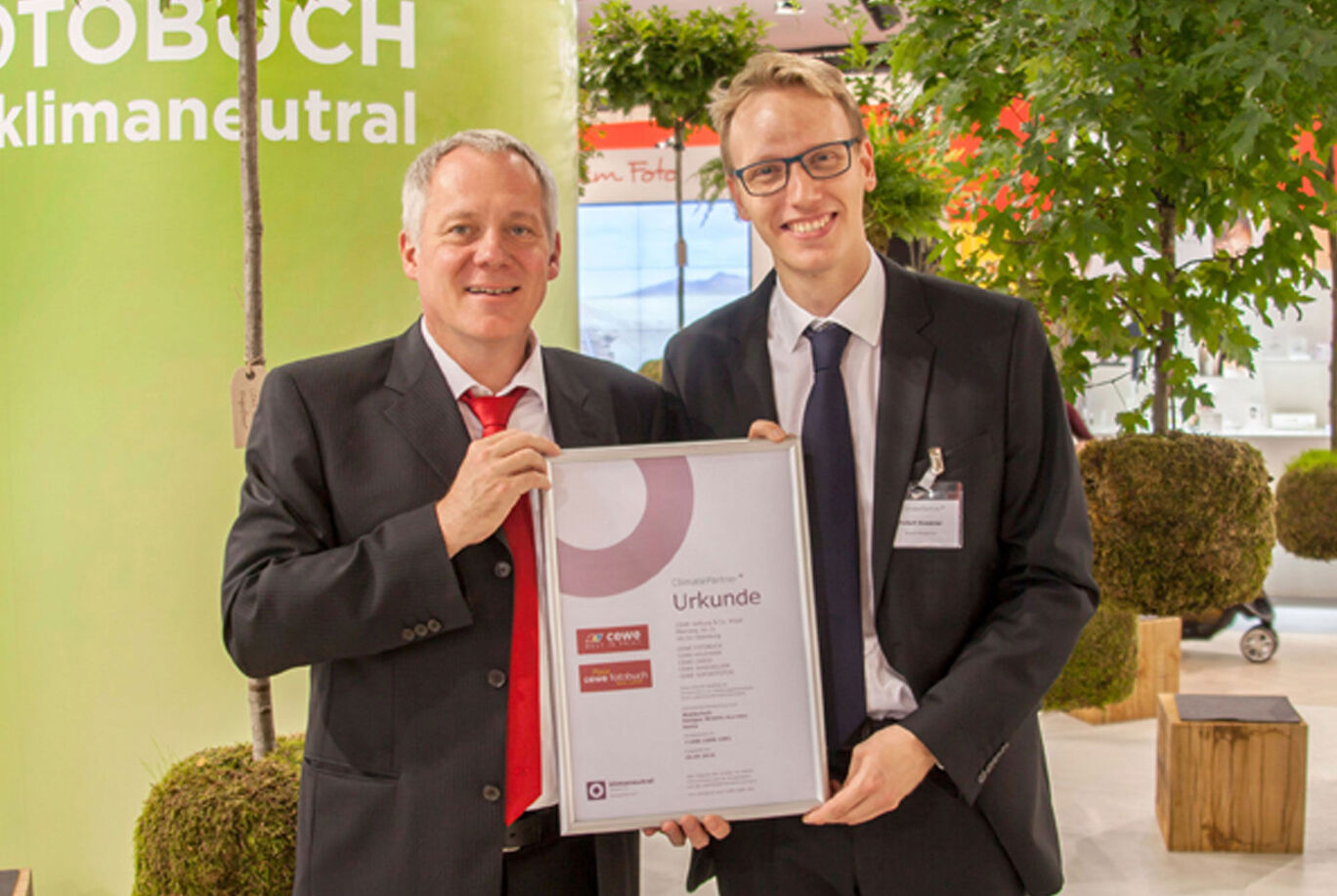 Two people hold a certificate for the CEWE photo book with the word "Certificate".