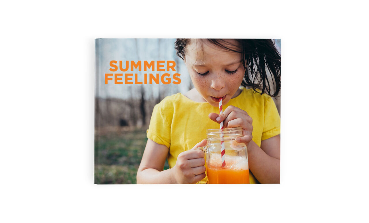 A child holds a glass with an orange drink and enjoys summer. They are wearing a yellow T-shirt.