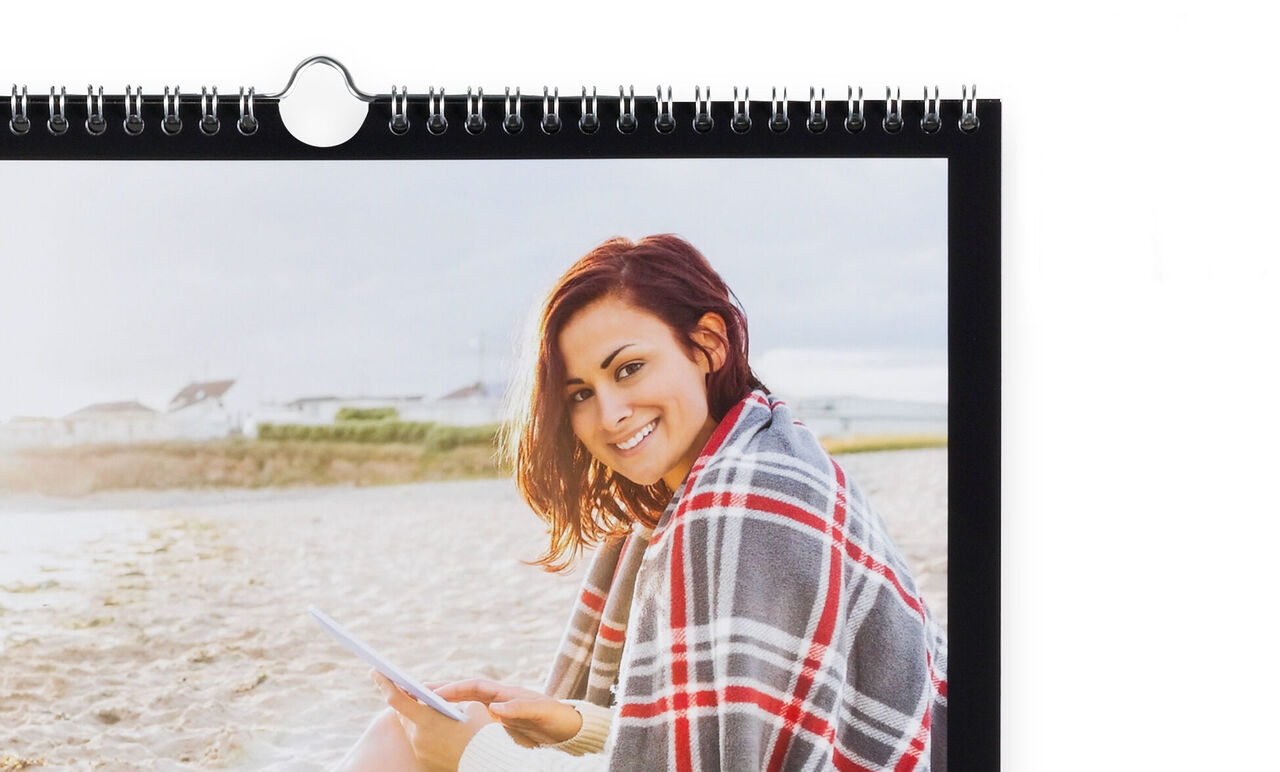 A person sits on the beach with a beautiful photo calendar, reading a book wrapped in a warm blanket.