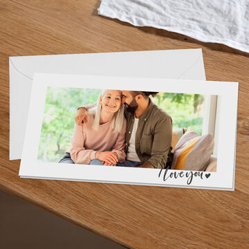 A couple sits on the couch enjoying a loving moment while looking at a greeting card