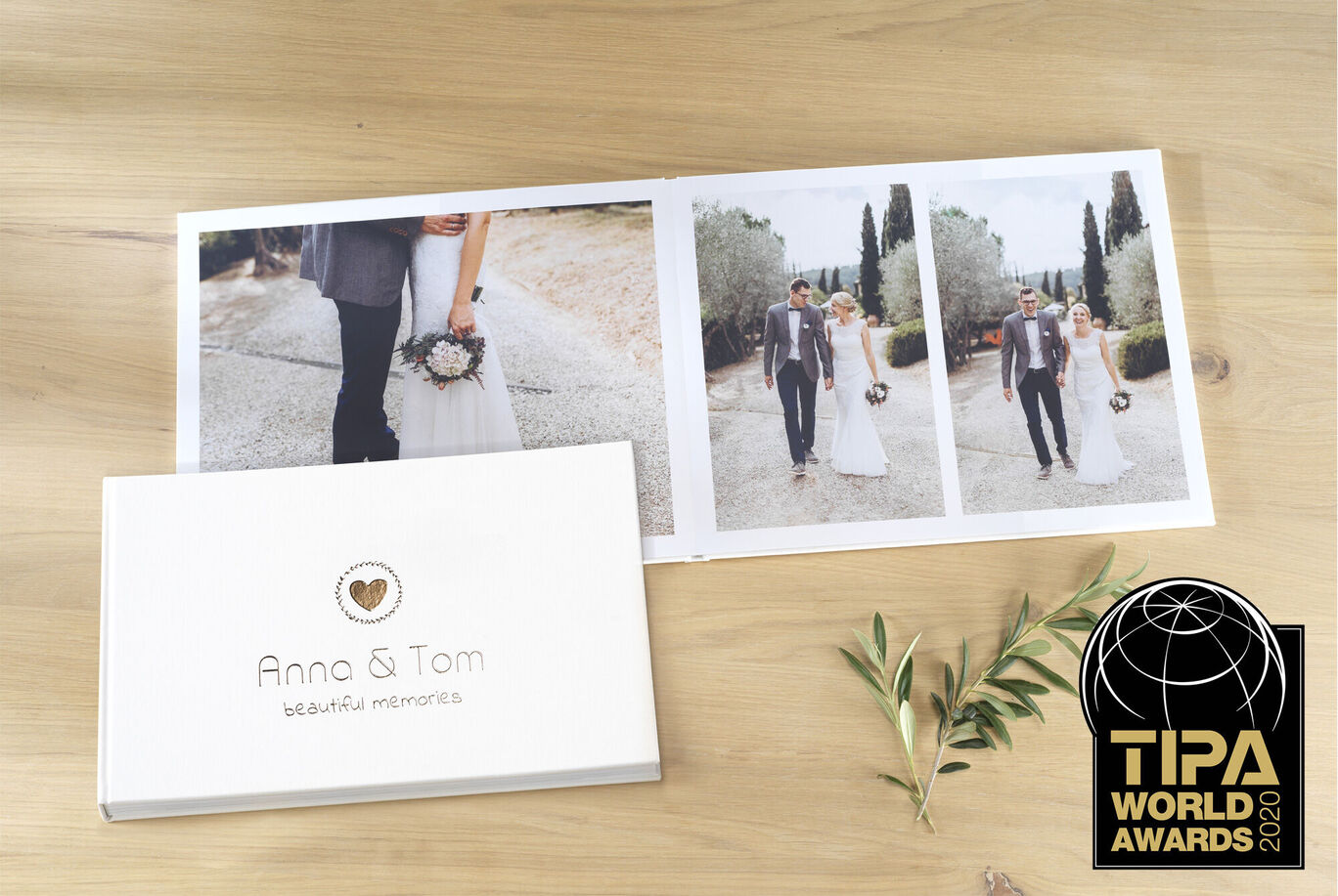 A high-quality CEWE PHOTO BOOK featuring the names Anna & Tom and three wedding images displayed on a wooden plate.