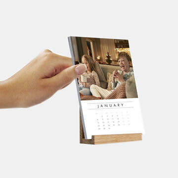 Holding a photo calendar for January while cheerful people sit on the sofa