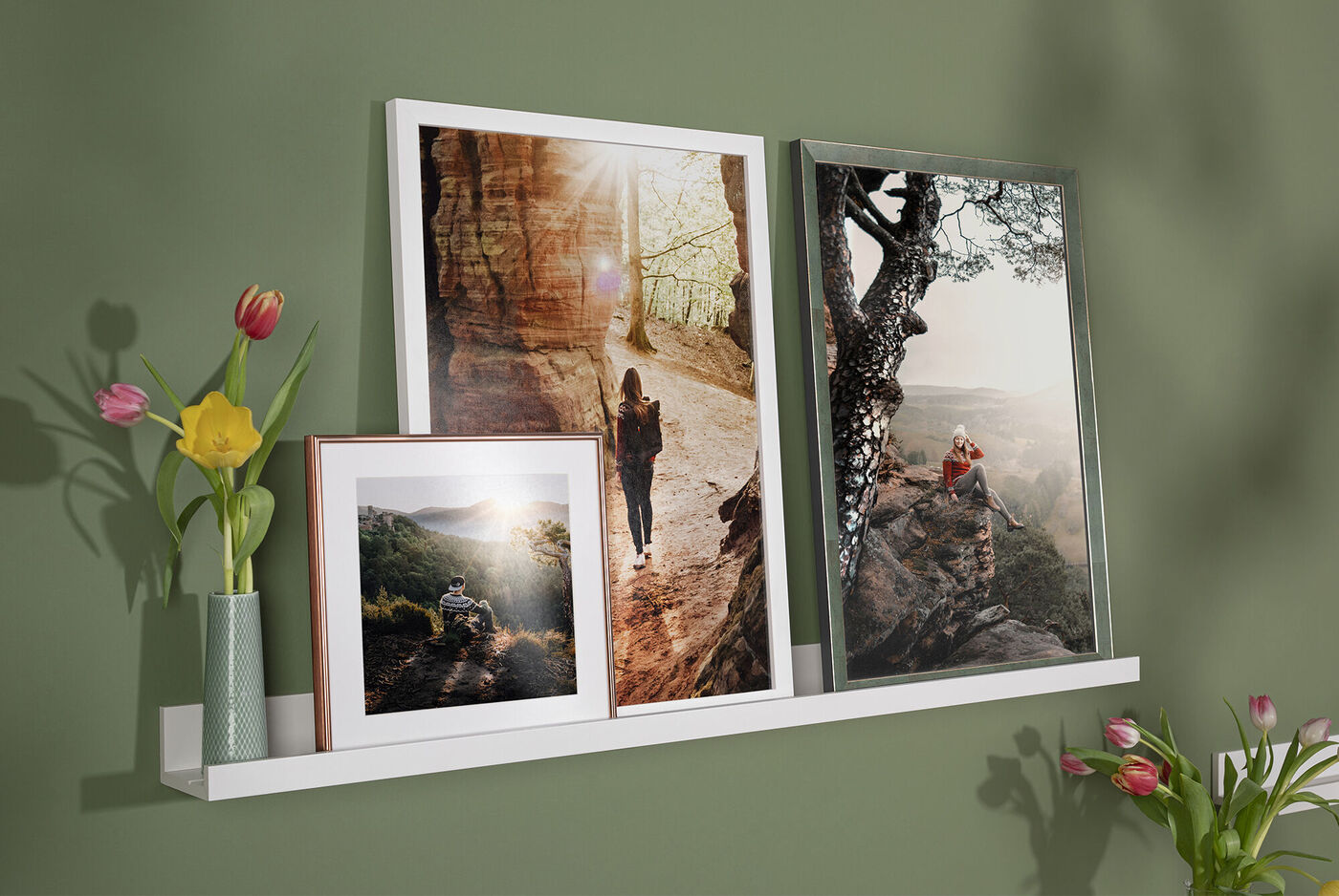 Three pictures in frames on a shelf, with flower vases beside them.