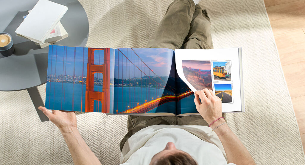Person flips through a CEWE photo book with images of the Golden Gate Bridge and travel moments.