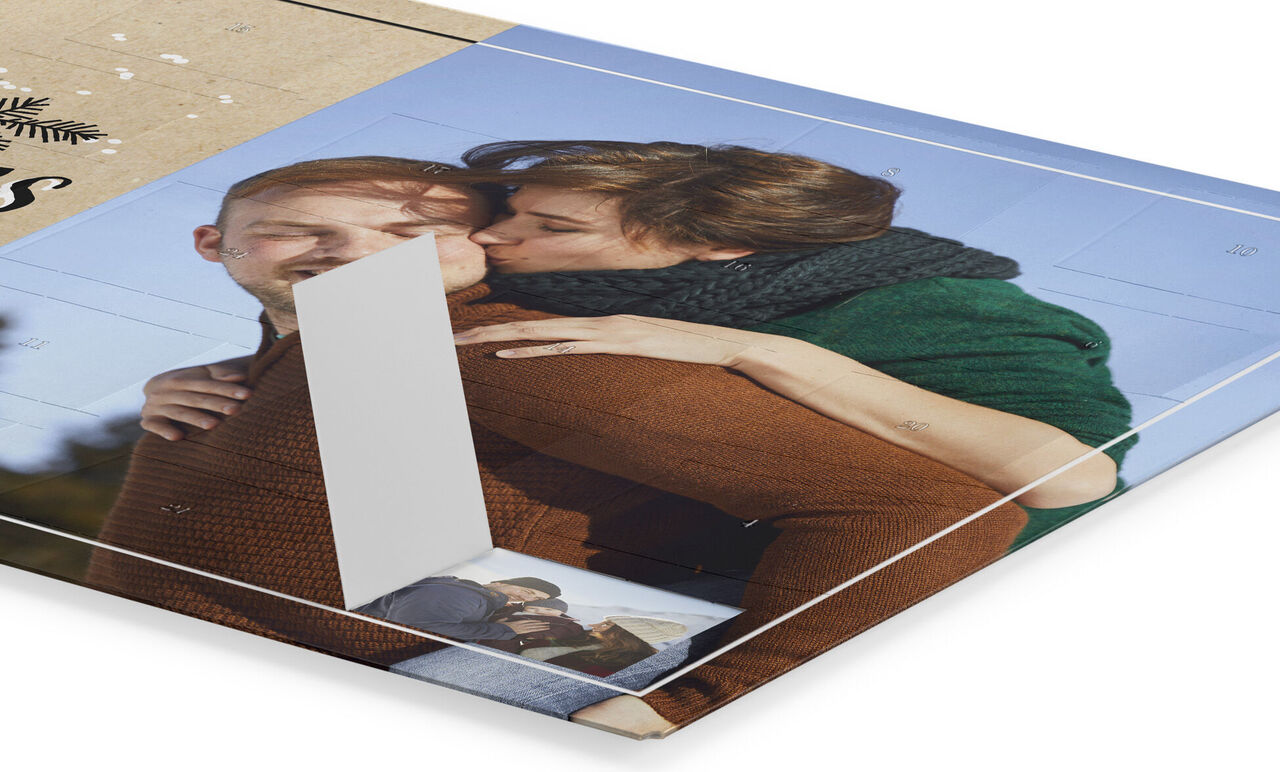 A woman hugs a man from behind and kisses his cheek. The background shows a photo book with pictures capturing memories.