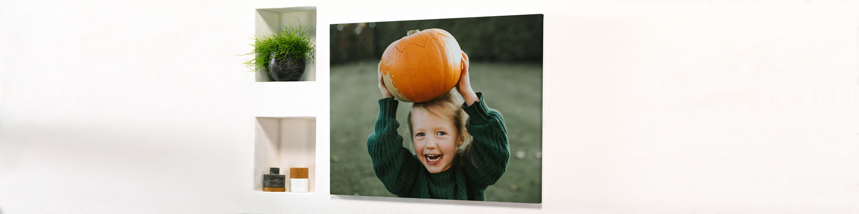 A child holds a large orange pumpkin over its head.
