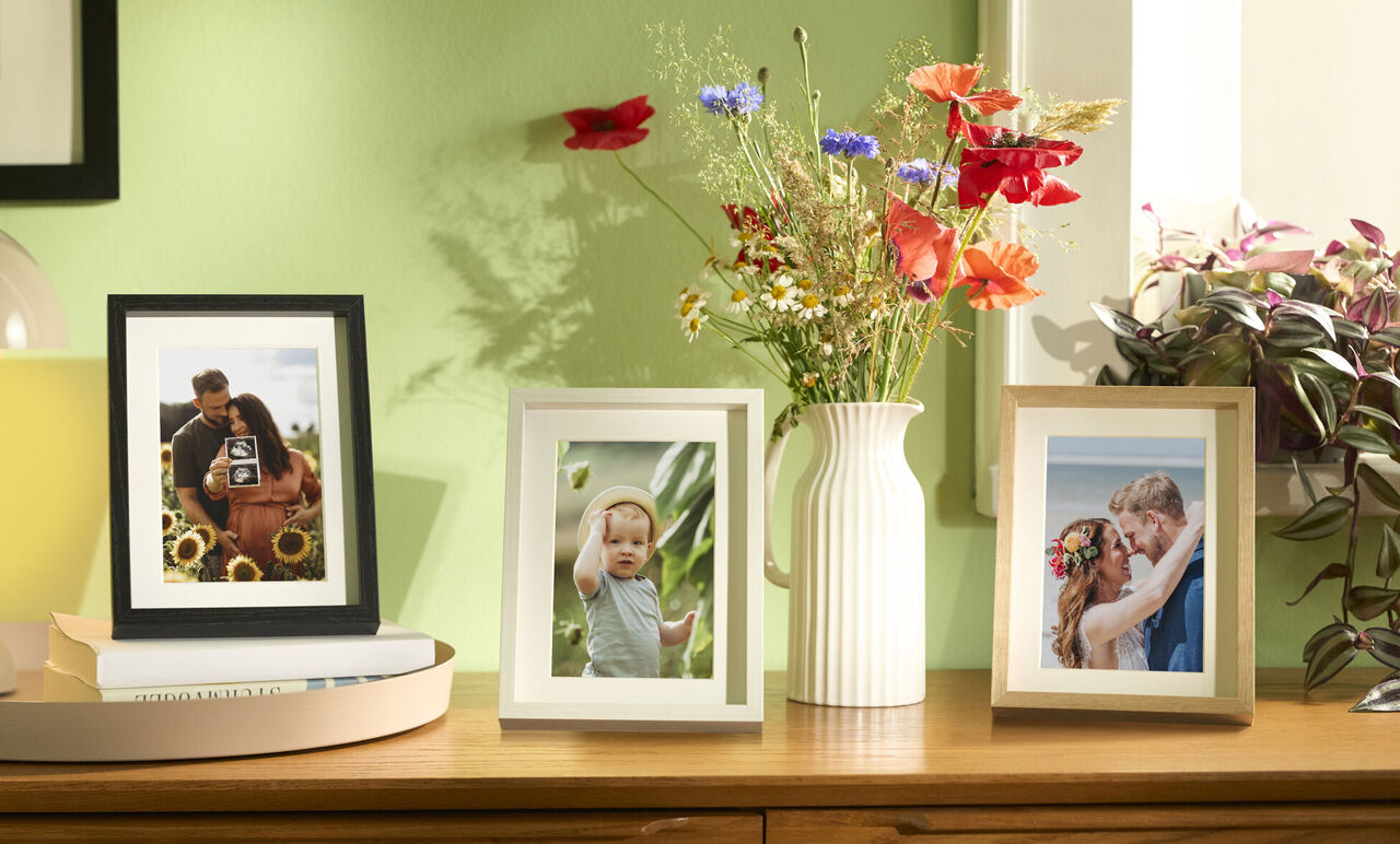 Three picture frames with photos and flowers in a bright setting.