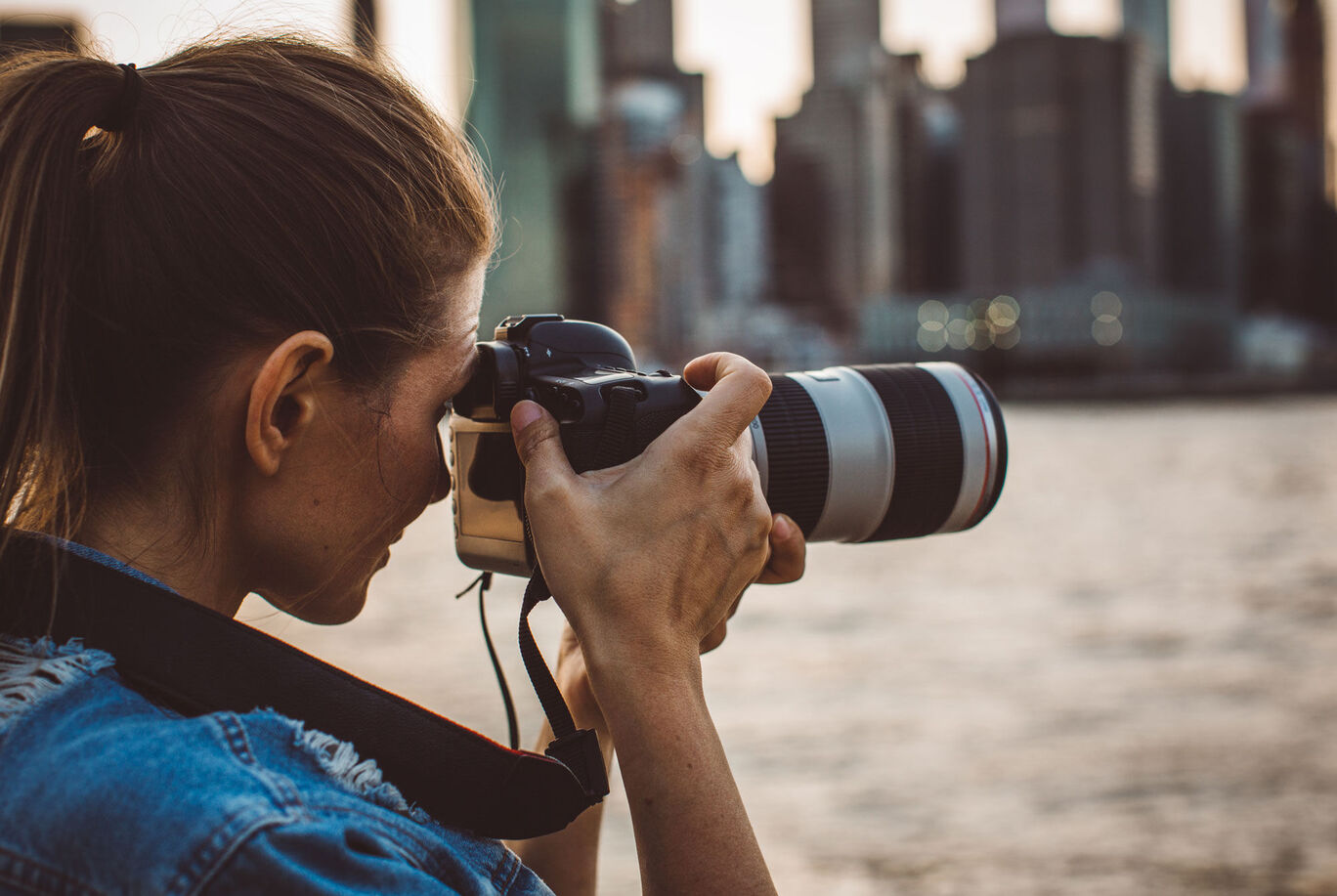 A person with a camera photographing a city view by the water.